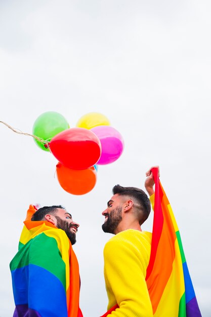 Casal masculino alegre cobrindo na bandeira do arco-íris na parada do orgulho gay