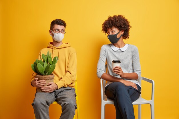 Casal mestiço usa máscaras protetoras, mantém distância, olha um para o outro, evita que o coronavírus espalhe pose nas cadeiras