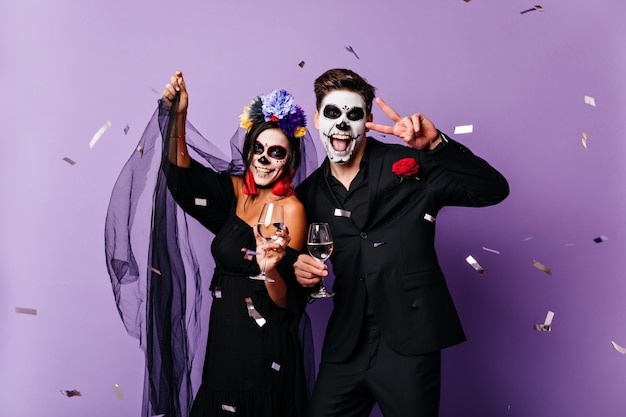 Casal morto bebendo champanhe no halloween. adorável noiva zumbi se divertindo na festa com o namorado.