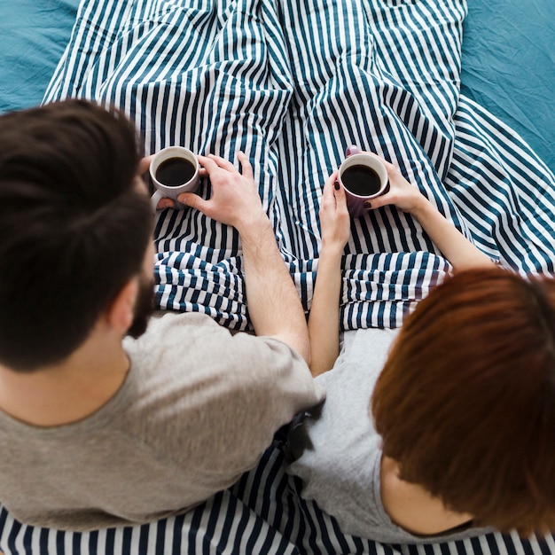 Casal na cama segurando xícaras de café