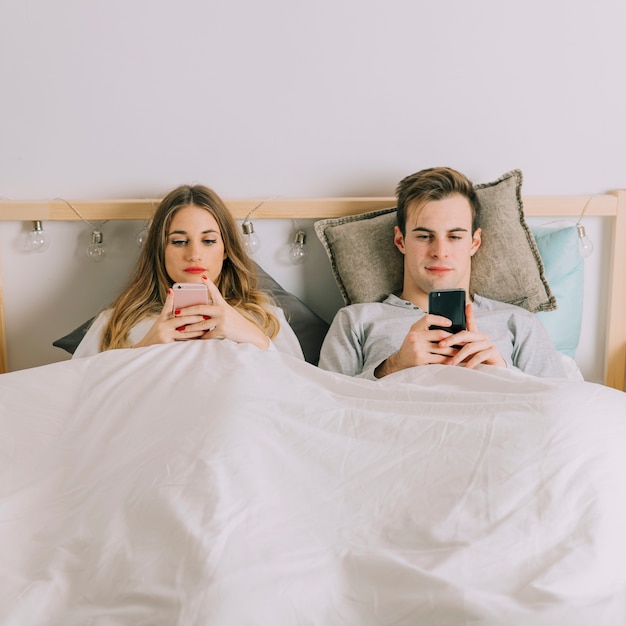 Foto grátis casal navegando telefones na cama