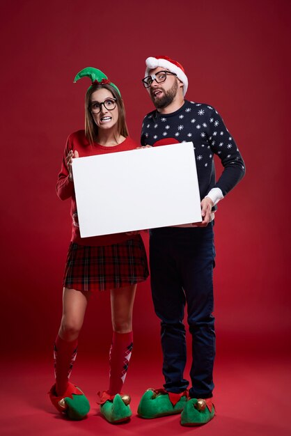 Casal nerd feliz com roupas de Natal segurando um papel em branco