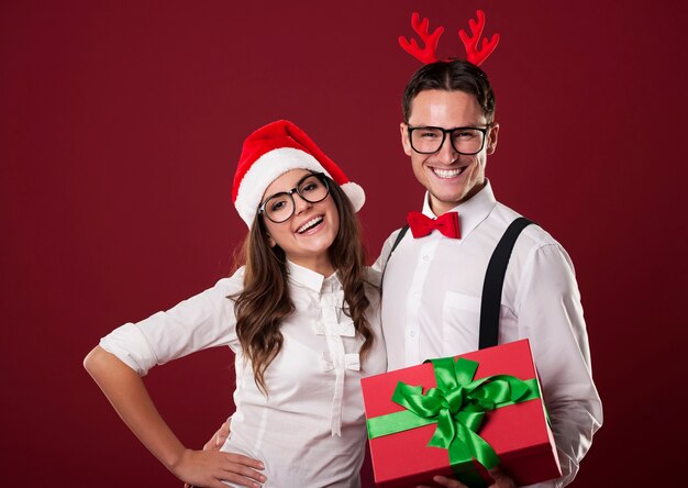 Casal nerd sorridente segurando um presente de Natal vermelho