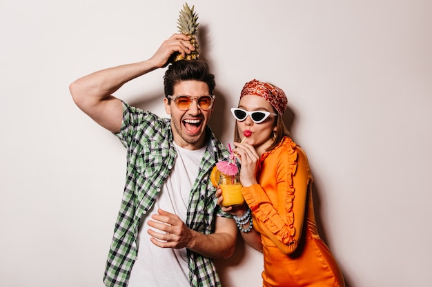 Casal otimista com roupa elegante de verão está descansando e saboreando um coquetel e abacaxi.