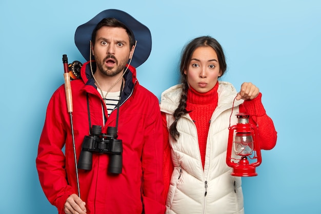 Foto grátis casal passa o fim de semana junto na natureza, vai pescar à noite, leva lampião a querosene e vara de pescar, usa roupas casuais quentes, fica de pé sobre a parede azul