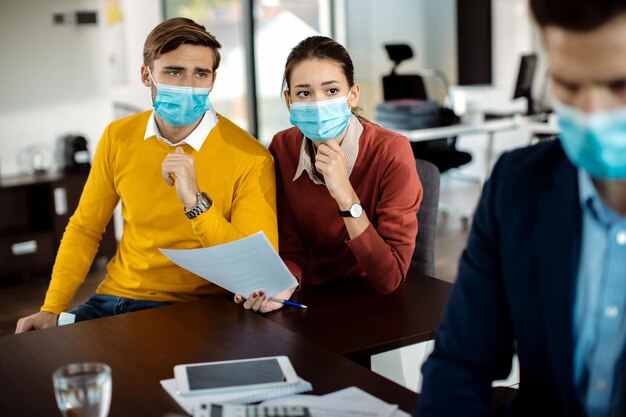 Casal perturbado analisando a papelada enquanto se encontra com o gerente do banco durante a pandemia de coronavírus