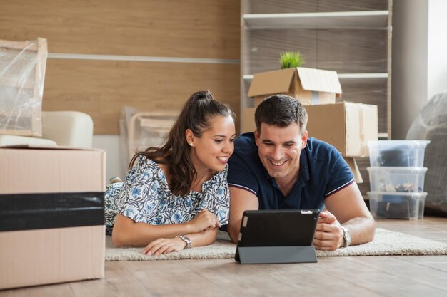 Casal planejando decoração on-line com um tablet e se mudando para casa na sala de estar. Jovem casal se mudando para o novo apartamento.