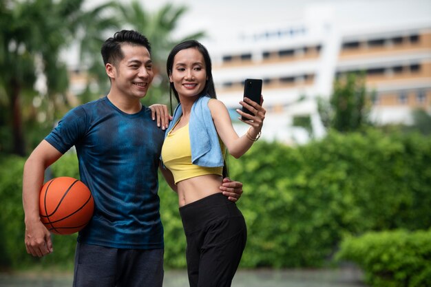 Casal posando juntos ao ar livre para uma selfie com basquete