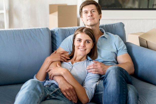 Casal posando no sofá enquanto faz as malas para mudar de casa