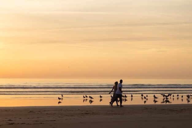 Casal quente caminhando na praia ao pôr do sol. Homem e mulher em roupas casuais correndo ao longo da água ao entardecer. Amor, família, conceito de natureza