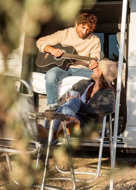 Casal relaxando e tocando violão ao lado do carro durante uma viagem