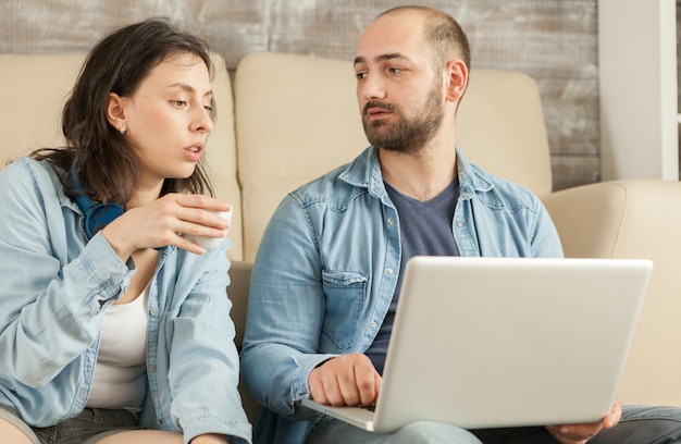 Casal relaxando na sala de estar tomando café e navegando na internet