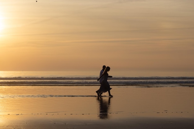 Casal romântico caminhando na praia ao pôr do sol. Homem e mulher em roupas casuais passeando pela água ao entardecer. Amor, família, conceito de natureza