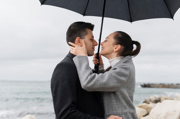 Casal romântico de tiro médio com guarda-chuva