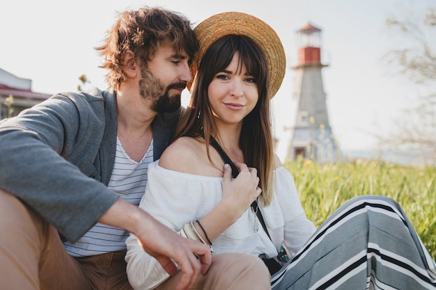 Casal romântico jovem hippie estilo indie apaixonado caminhando pelo campo, farol no fundo, férias de verão