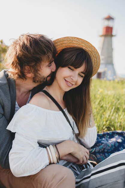 Casal romântico jovem hippie estilo indie apaixonado caminhando pelo campo, farol no fundo, férias de verão