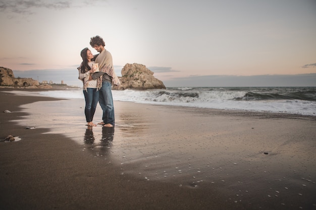 Casal se abraçando na costa da praia segurando uma vela