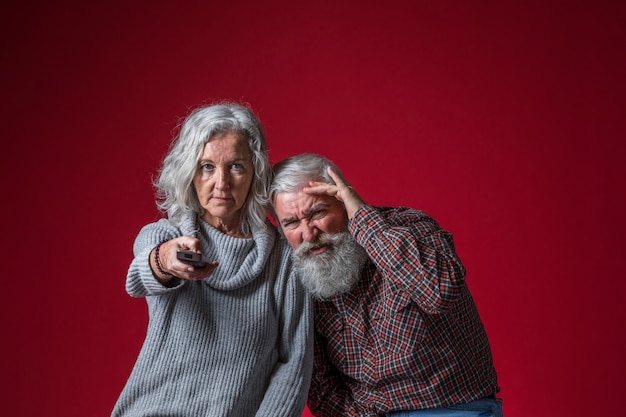 Foto grátis casal sênior assistindo a televisão juntos contra o fundo vermelho