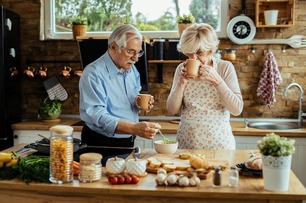 Casal sênior cozinhando comida saudável e tomando café na cozinha.