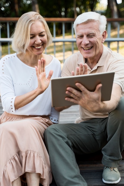 Foto grátis casal sênior sorridente acenando para um tablet ao ar livre