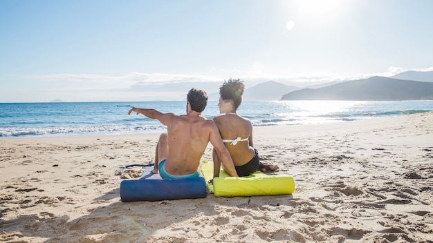 Casal sentado e apontando para a praia