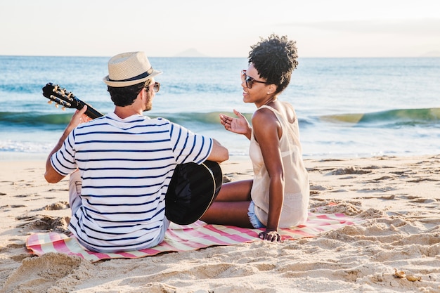 Casal sentado na areia com guitarra