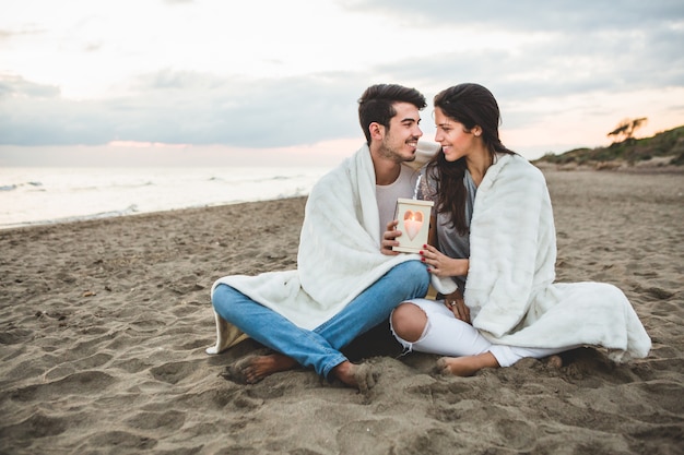 Casal sentado na areia com uma vela e um cobertor