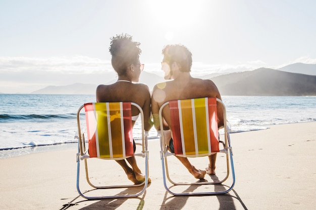 Foto grátis casal sentado na cadeira do convés na praia