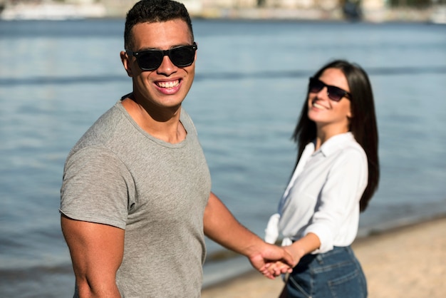 Casal sorridente com óculos escuros de mãos dadas na praia