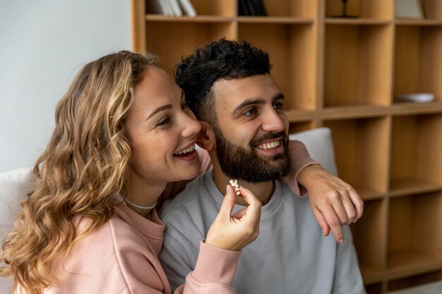 Casal sorridente comendo pipoca e assistindo filme em casa