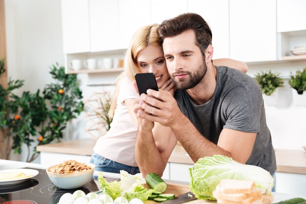 Casal sorridente feliz usando telefone celular para encontrar uma receita