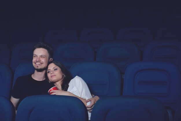 Casal sorridente se abraçando e assistindo filme engraçado no cinema
