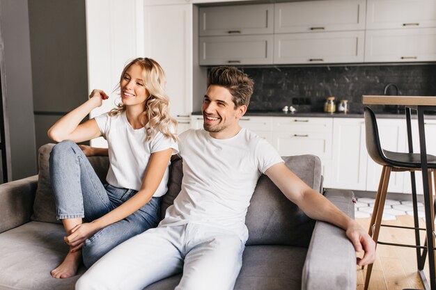 Casal sorridente, sentado no sofá em apartamentos modernos e assistindo tv. Jovem alegre com sua linda namorada relaxando em casa.