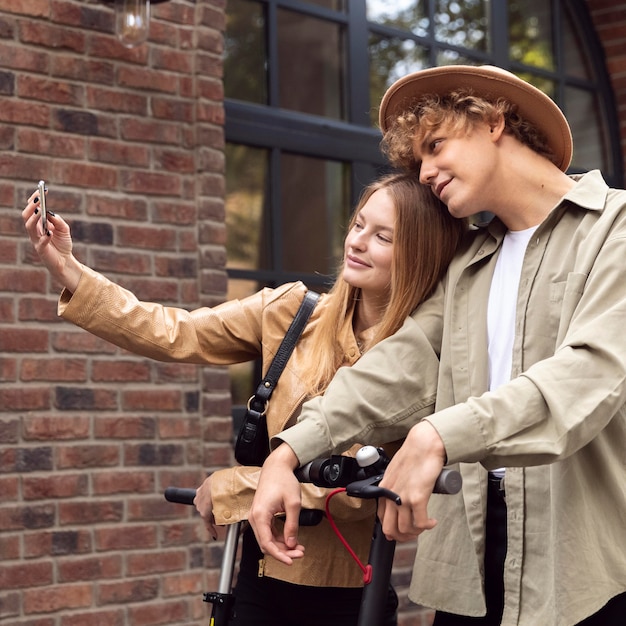 Foto grátis casal tirando selfie ao ar livre com scooters elétricos