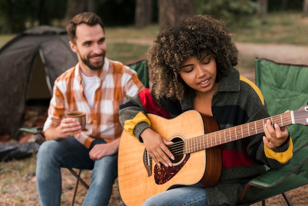 Casal tocando violão enquanto acampa ao ar livre