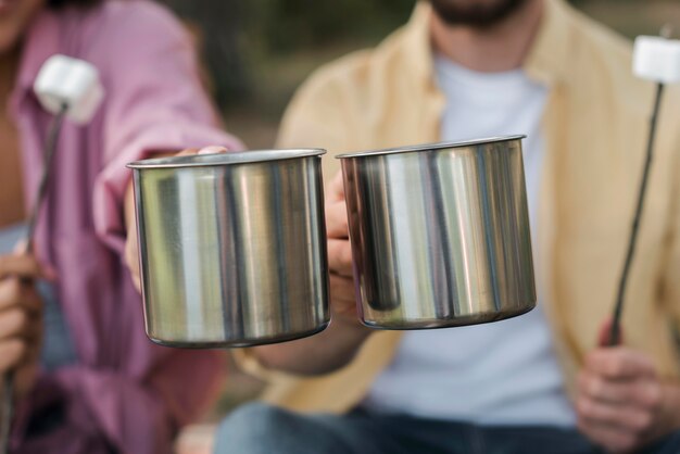 Casal tomando marshmallows e bebidas quentes enquanto acampa