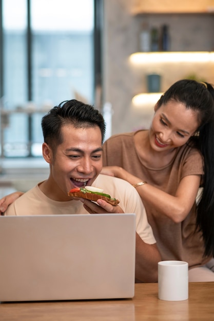 Casal trabalhando em casa no laptop enquanto toma café e sanduíche