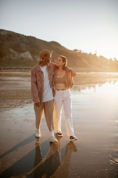 Casal trans abraçados e caminhando na praia ao pôr do sol