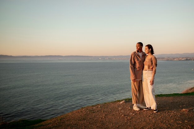 Casal trans abraçados na praia enquanto observa o pôr do sol