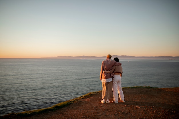 Casal trans assistindo o pôr do sol na praia e abraçados