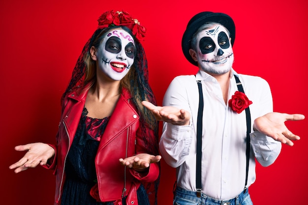 Casal vestindo fantasia de dia dos mortos sobre vermelho sorrindo fazendo  moldura com mãos e dedos com cara de feliz. conceito de criatividade e  fotografia.