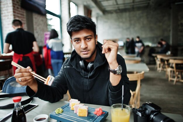 Casual e elegante jovem asiática com fones de ouvido no café comendo sushi