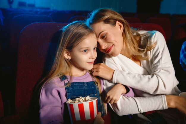 Caucasiana mãe e filha assistindo a um filme no cinema, casa ou cinema. Parece expressivo, surpreso e emocionado. Sentado sozinho e se divertindo. Relação, amor, família, infância, fim de semana.