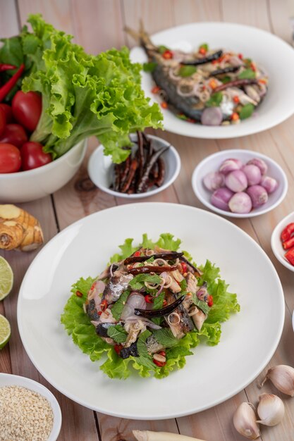 Cavala frita coberta com galanga, pimenta, hortelã, cebola vermelha em um prato branco.