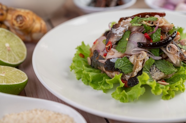 Cavala frita coberta com galanga, pimenta, hortelã, cebola vermelha em um prato branco.