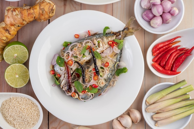 Cavala frita coberta com galanga, pimenta, hortelã, cebola vermelha em um prato branco.