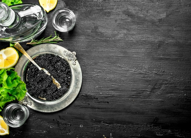 Caviar preto com vodka e rodelas de limão. em um quadro negro. Foto Premium