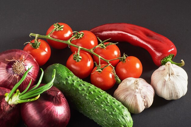 Cebola azul e alho, tomate e pepino em um preto.