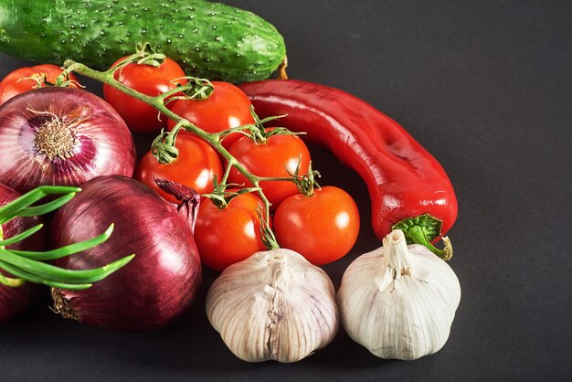 Cebola azul e alho, tomate e pepino em um preto.