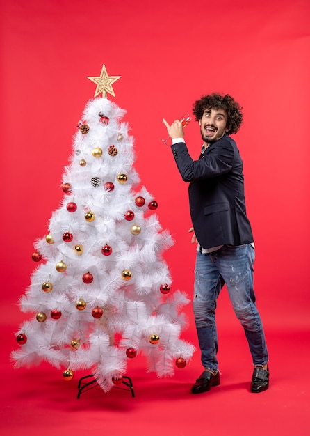 Celebração de ano novo com um jovem barbudo bebendo vinho e perto da árvore de natal branca decorada